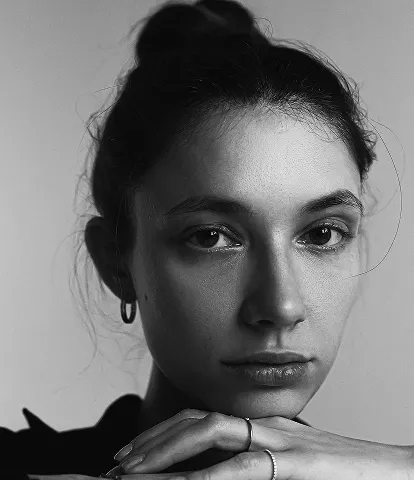 Black and white portrait of a woman with dark hair in an updo, looking directly at camera with hand near chin