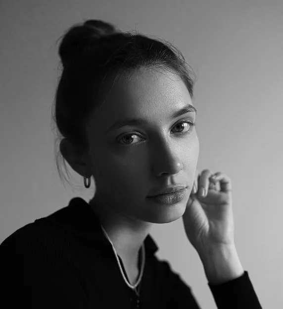 Black and white portrait of woman with hair in bun, hand near face, wearing dark clothing, looking directly at camera with thoughtful expression